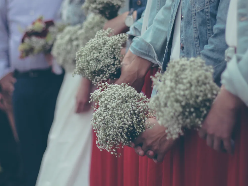 A row of wedding guests in varied attire holding small white bouquets