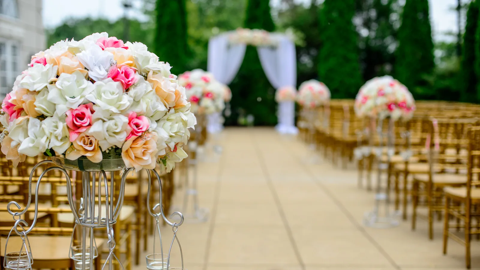 A decorated outdoor wedding aisle lined with floral arrangements leading to an arch